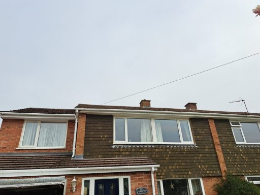 Two storey house with a flat roof, light brick and dark wood cladding, under a cloudy sky.