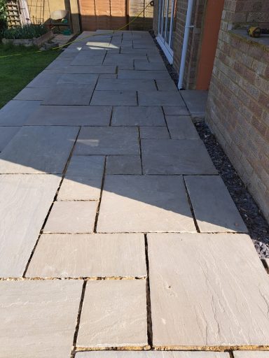 Paved pathway leading to a house, lined with grass on one side.