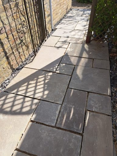 Pathway with stone slabs, sunlight creating shadows from a nearby fence.