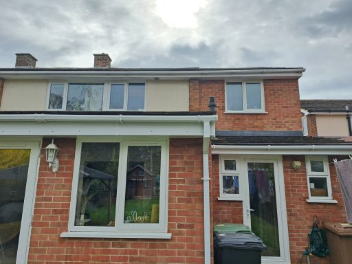 Brick house exterior with large windows and a green bin in the garden. Overcast sky above.