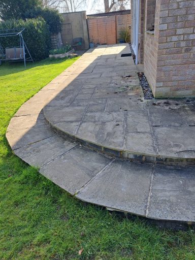 Paved patio with a curved edge, green grass, and a wooden gate in the background.