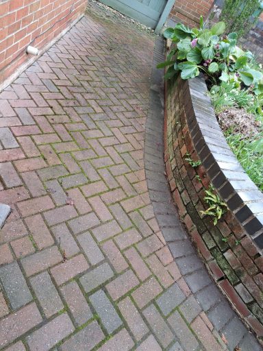 A curved brick pathway leading to a door, bordered by a stone planter.