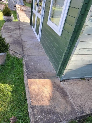 Concrete pathway beside a green wooden building, with grass alongside.