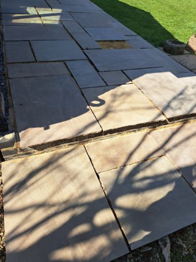 Irregularly laid stone patio with shadows cast from nearby trees.