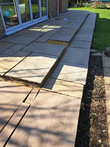 Stone patio with uneven slabs leading to a house and grassy area.
