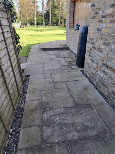 Paved path beside a stone wall leading to an open grassy area.