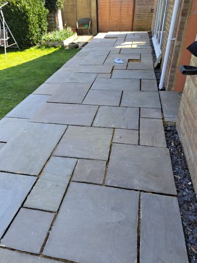 Paved terrace featuring large, rectangular stone slabs and a neatly maintained lawn.