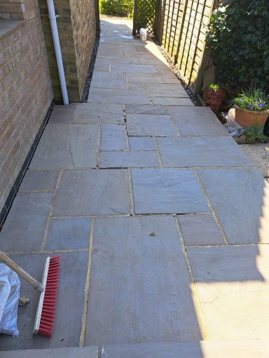 Paved walkway with uneven stone tiles and a broom on the side.